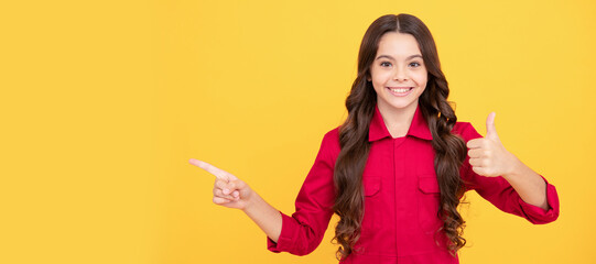 cheerful child girl pointing finger on copy space with thumb up gesture, success. Child face,...