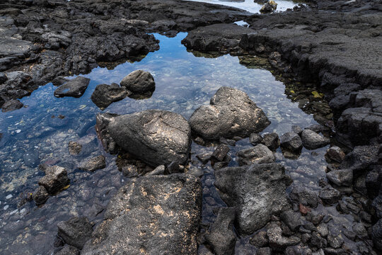 black lava rock and stones above and below coastal sea water