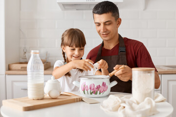 Image of happy family father and kid sitting at table in kitchen, daughter and dad cooking...