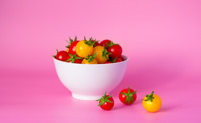 Red and yellow cherry tomatoes in a white bowl on a bright pink background. Horizontal photography. Copy space.