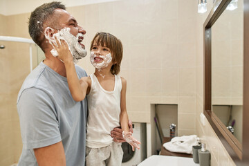 Son smear shaving foam on father beard in bathroom