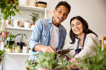 Small business plant shop owners looking at the camera while holding digital tablet