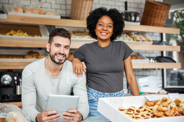 Bakery owners standing behind counter while holding digital tablet