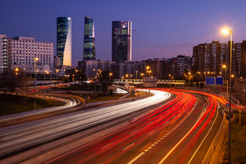Obraz na płótnie Canvas Long exposure traffic lights at sunset in Madrid street with big towers in the background