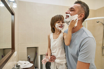 Little son smearing shaving foam on father beard