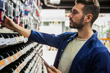 Male hardware shop worker taking inventory on digital tablet