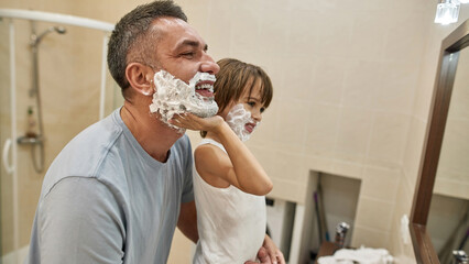 Little boy and father smear shaving foam on faces