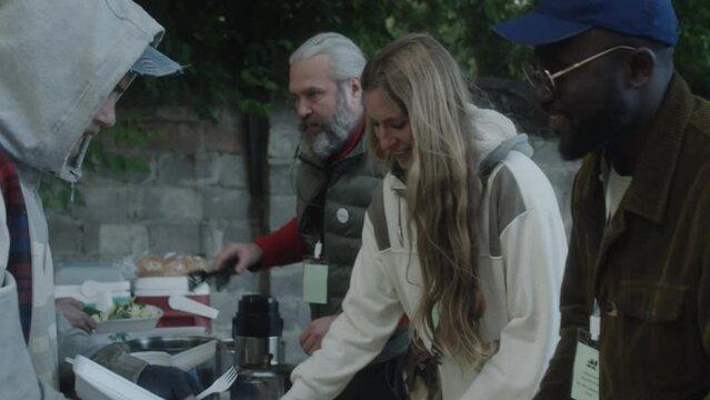 Multiethnic volunteers giving free food to homeless people on outdoor soup kitchen