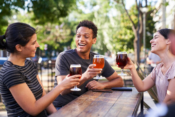 Mid-shot photo three young diverse friends raising their beers to make a toast at happy hour