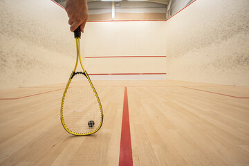 Male hand holding a racket inside a squash court. Low angle, unrecognizable person, large depth of...