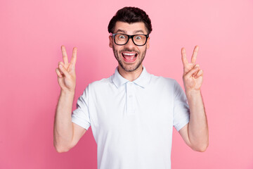 Portrait photo of young attractive handsome funny man wear eyeglasses showing v-sign two hands positive excited good mood isolated on pink color background