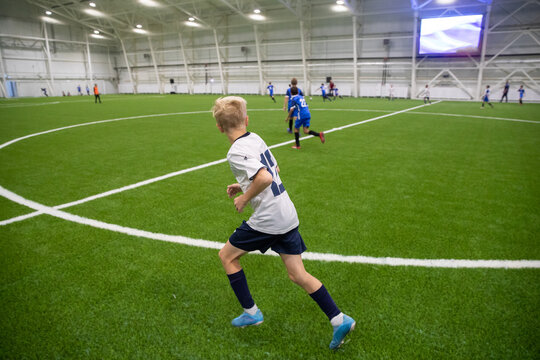 Young soccer player running on new artificial grass football field. Sports hall for football at any time of the year. The football field is covered with artificial grass, lighting spotlights are insta