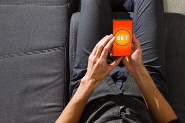 hands of a man holding a online betting device. All screen graphics are made up.