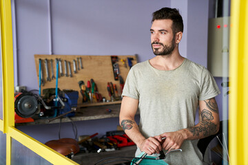 Medium-shot  of bearded mechanic standing in his workshop in front of his tools