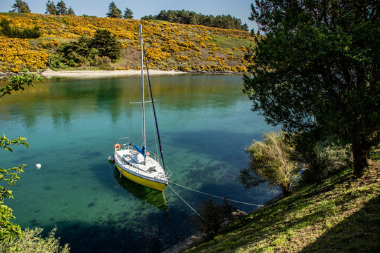 A small wooden sailboat moored on flat calm water in a cove