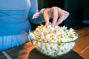 Girl reaches for the popcorn in a glass cup in the kitchen. Getting ready to watch a movie