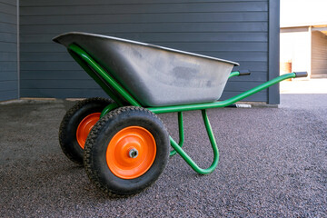A garden wheelbarrow with bright wheels stands in the yard. Working Garden appliance - obrazy, fototapety, plakaty