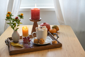 Obraz na płótnie Canvas Hot chocolate drink with melting marshmallows, muffins, candles, flowers and autumn pumpkins on a table at the window, copy space, selected focus
