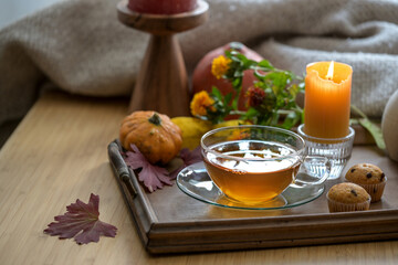 Healthy hot tea against cold and flu on a wooden tray with cookies, candle and autumn decoration, selected focus
