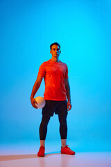 Full-length portrait of male volleyball player posing with ball isolated on blue studio background...