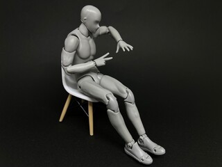 椅子に座って1人でじゃんけんをする人形。ひとり遊び、暇つぶしのイメージ。