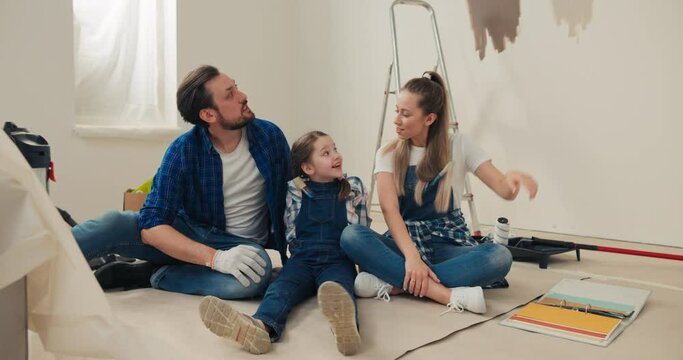 The happy owners of the new apartment are happy because the renovation they have long dreamed of has begun. Man wife and child sitting on floor telling visions of colors pointing a finger at walls.