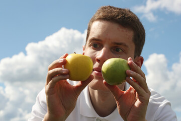 Young man with green and yellow apples in hands on a blue sky background. Pavel Kubarkov, two...
