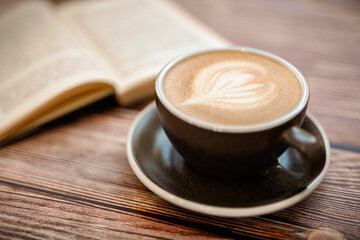 A Cup of hot soya latte art coffee on wooden table with book in coffee shop 