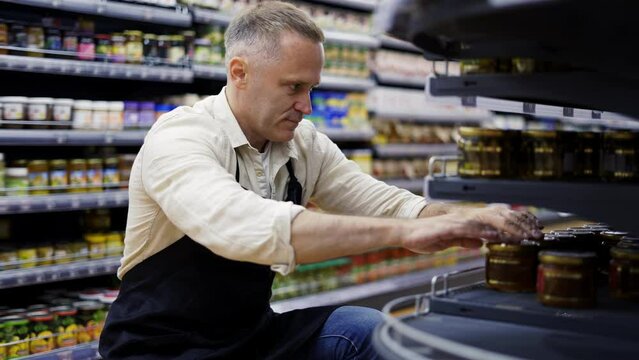 A middle-aged grocery store worker controls the placement of goods on the shelves. Goods control. The concept of working in a supermarket