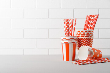 Pile of red paper cups and striped straws for birthday party. Brick wall. Pop Art style. Space for text