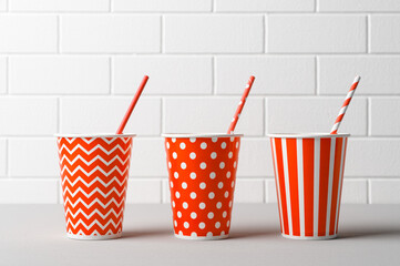 Three red paper cups and striped straws for birthday party. Brick wall. Pop Art style.