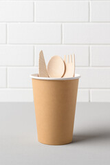 Eco friendly wooden cutlery in craft paper cup on the brick wall background. Recycling eco concept. Space for text