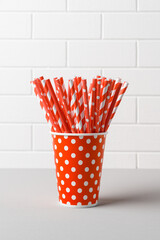 Pile of red striped straws in paper cup for birthday party. Brick wall. Pop Art style. Space for text
