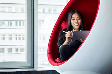 Young woman drawing on digital tablet at office sitting in chill zone in comfortable chair