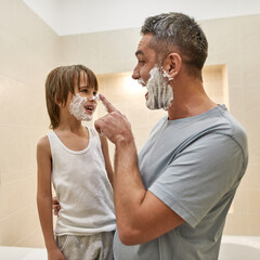 Father smearing foam on son nose during shaving