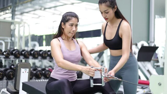 Fitness trainer motivate young active sport woman or athlete exercising using weight lifting machine, sculpt muscles, bodybuilding,  lose weight to increase mobility in gym.