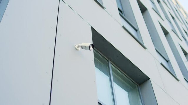 White CCTV security surveillance camera built into the metal wall of the modern glass office building outside. installed outdoor in city. Privacy, urban, protection, house system control, secure video