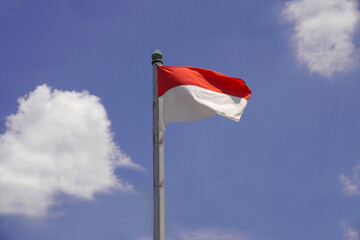 An Indonesian flag is flying with a blue cloudy sky background