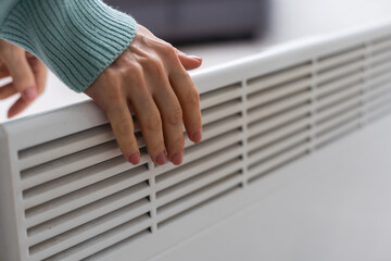 Woman's hand on a white radiator. Heating season. Energy crisis. Cold batteries. Central heating