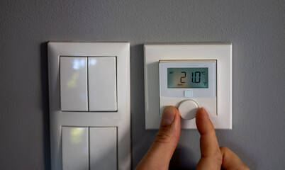 Hand changes the temperature to 21 degrees Celsius on a electronic thermostat. Symbol for saving...