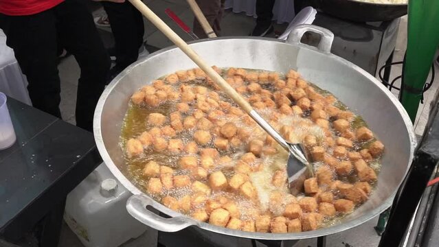 slow motion of chef is frying tofu in a large skillet.