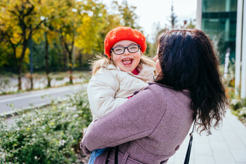 Fototapeta premium Cute little girl in a red beret with special needs enjoy having fun spending time with mother outdoor in aututm time. Happy family moments concept.