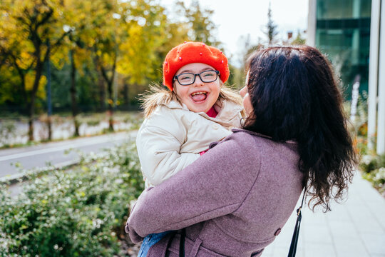 Cute little girl in a red beret with special needs enjoy having fun spending time with mother outdoor in aututm time. Happy family moments concept.