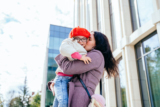 Cute little girl in red beret with special needs enjoy having fun spending time with mother outdoor in aututm time at city street. Happy family moments concept.