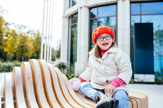 Happy family moments in the city. Photo portrait of little girl wearing red beret and coat sits at bench at city street outdoors.