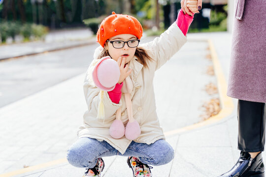 Cute girl in coat red beret in eyeglasses with special needs holding mother's hand on a walk outdoor.
