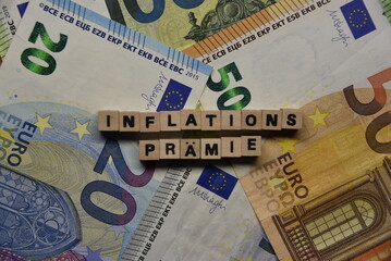 Das Wort Inflationsprämie mit Holzbuchstaben auf liegenden Euroscheinen