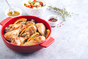 Chicken drumsticks with oranges and thyme baked in red round baking dish