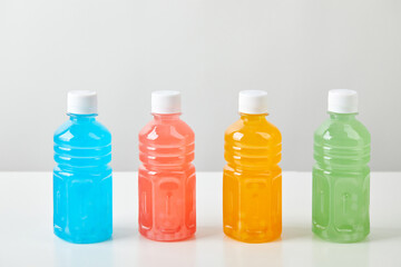 Four small bottles with colorful drinks on white background