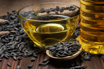 Sunflower oil in glass bowl and bottle with seed in wooden spoon on wooden background